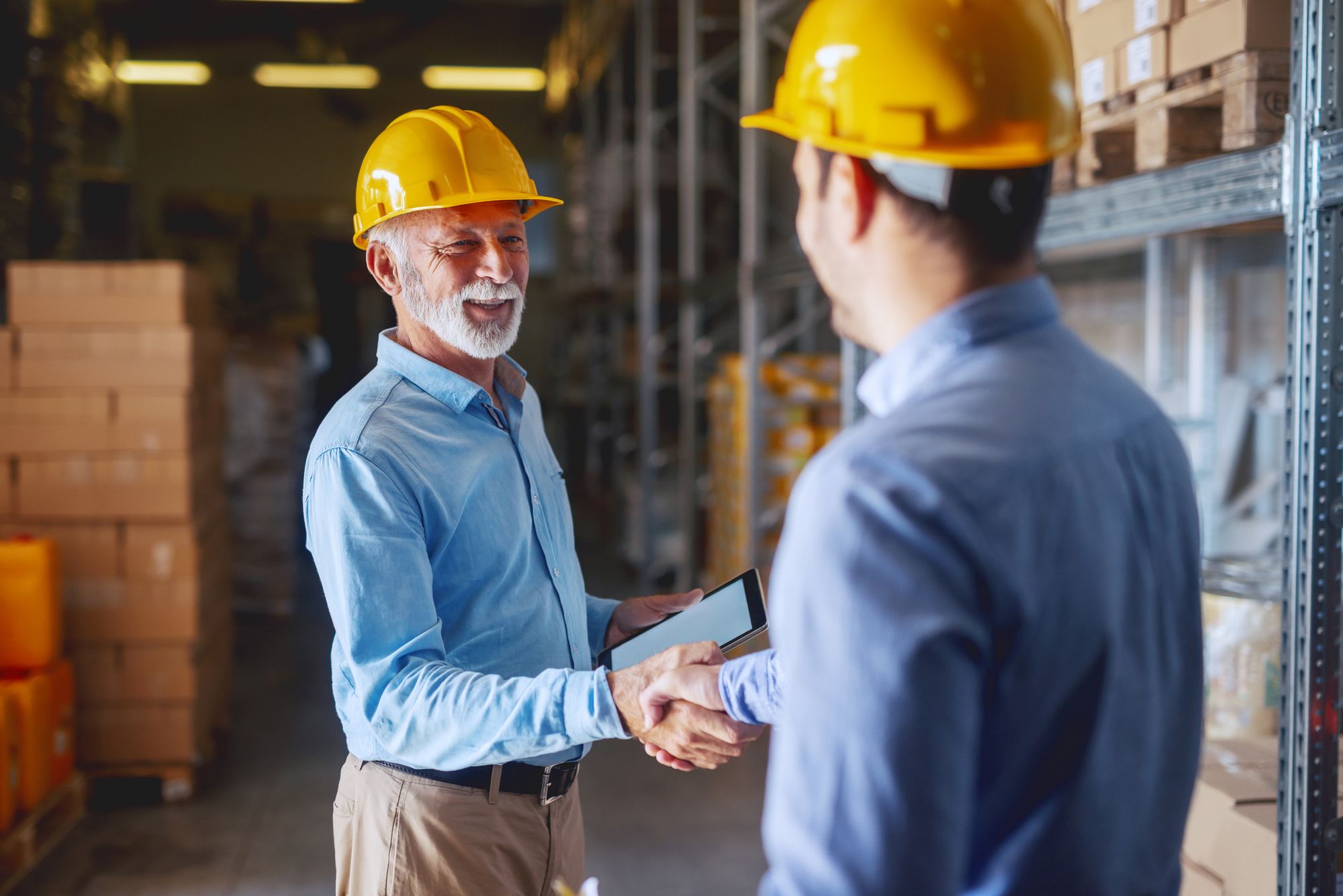 Two business partners shaking hands with a tablet PC on hand.