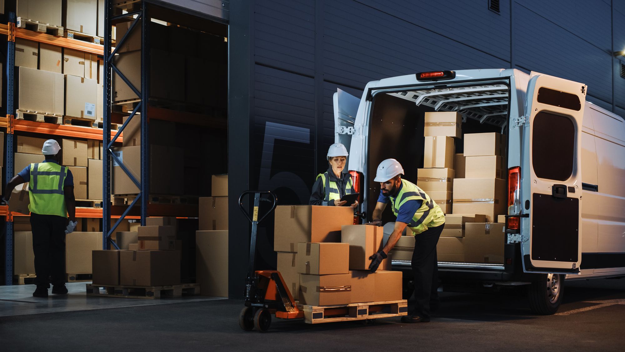 Workers moving product boxes to vehicles for delivery from the warehouse.